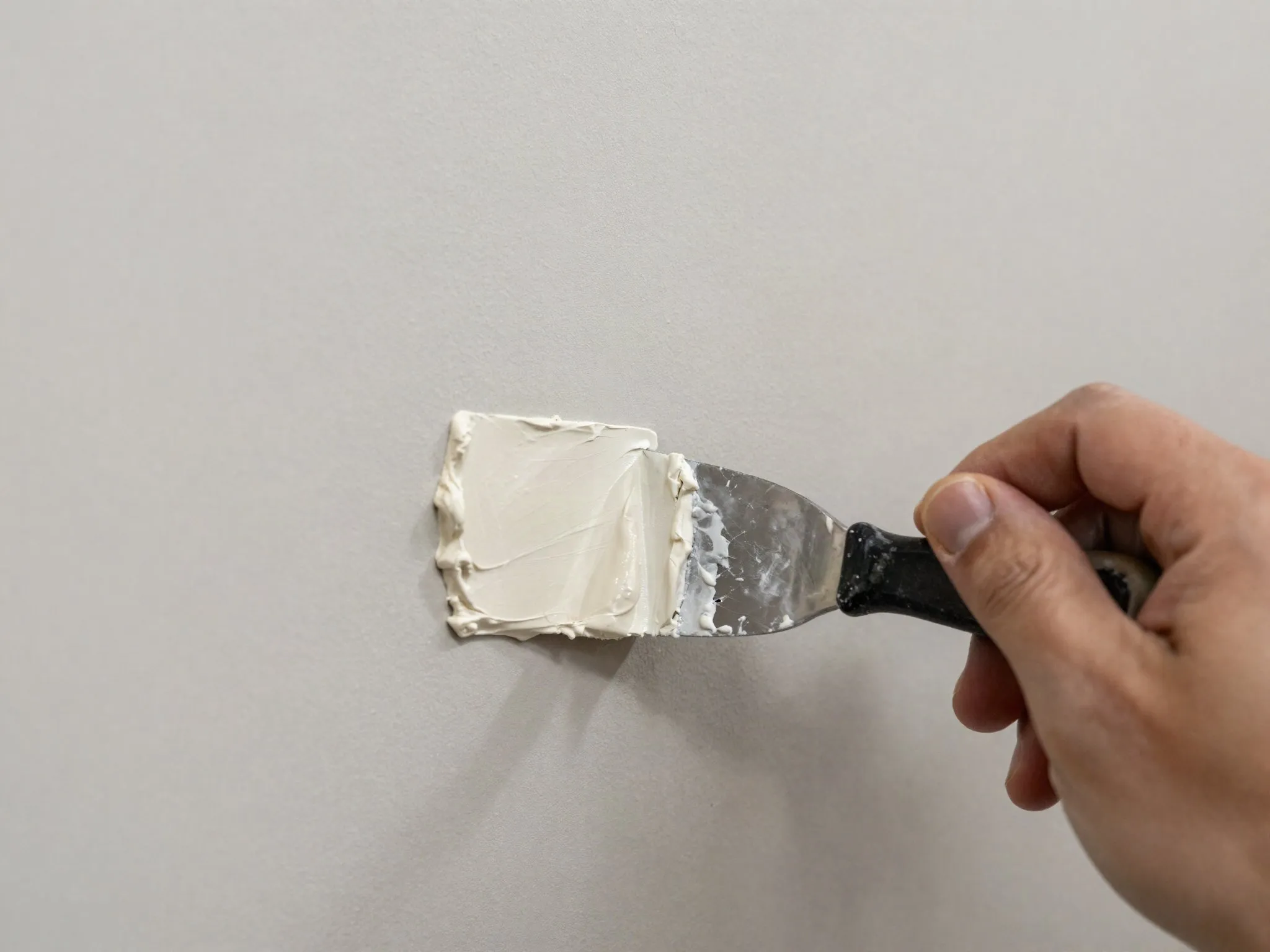 A hand spreading joint compound over a drywall patch with a putty knife